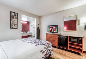 Una habitación de hotel con una cama, televisión, espejo, cómoda y microondas.
