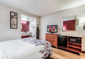 A hotel room with a bed, a television, a mirror, a dresser, and a microwave.