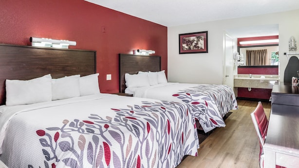 Een hotelkamer met twee bedden, een bureau en een zichtbare badkamer door een geopende deur.