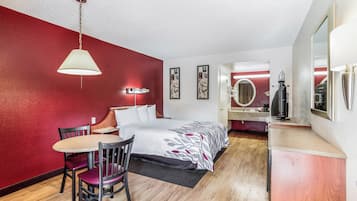 Habitación de hotel con cama, escritorio, silla, espejo y lámpara colgante.