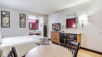 A hotel room with a bed, a desk with a television, a small refrigerator, and a mirror.