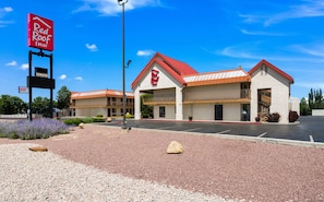Un Red Roof Inn con un edificio de dos pisos, un estacionamiento y un cielo azul despejado.