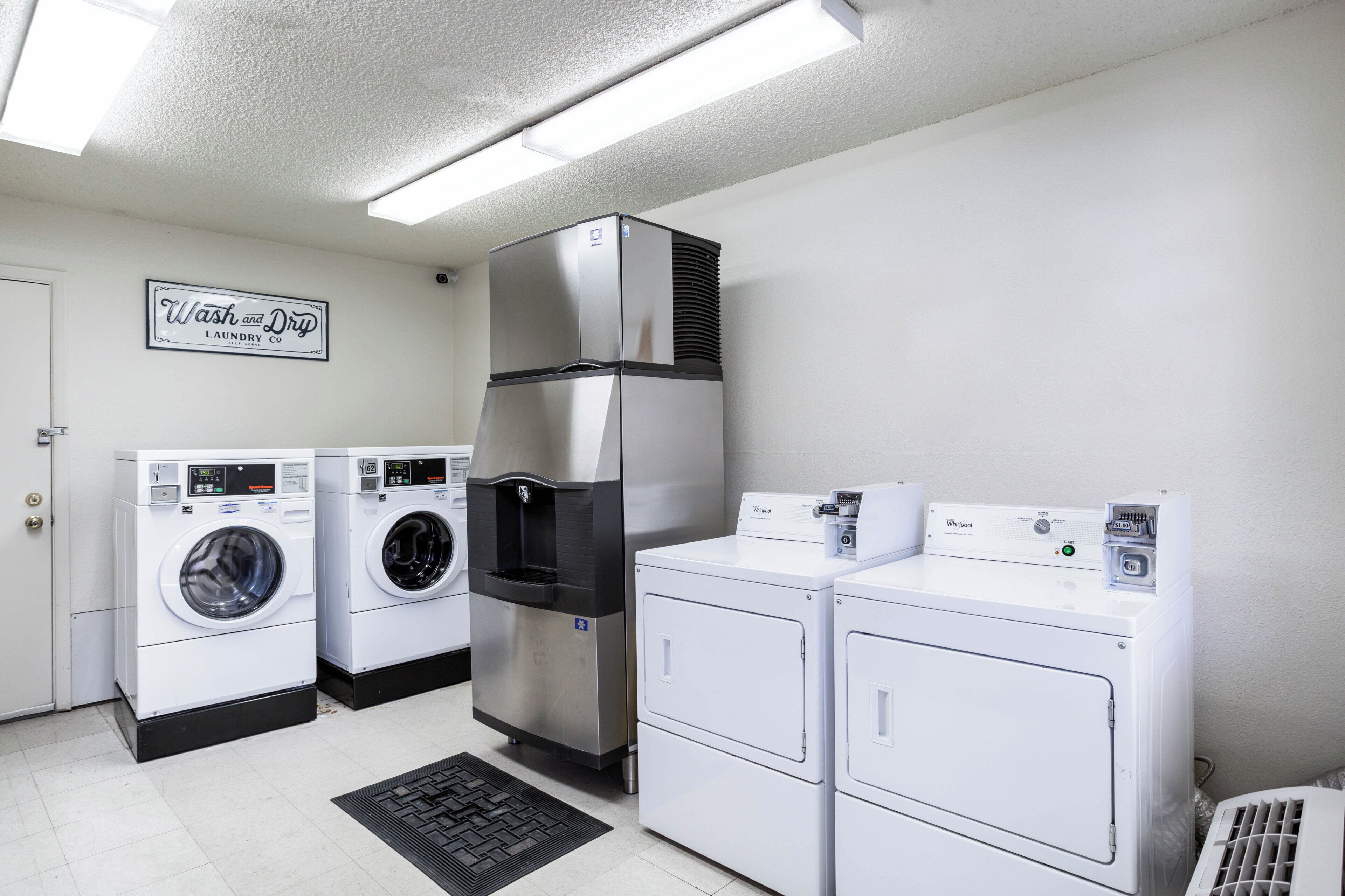 A laundry facility with a Whirlpool washer, a stacked washer and dryer unit, and a sign indicating self-service.
