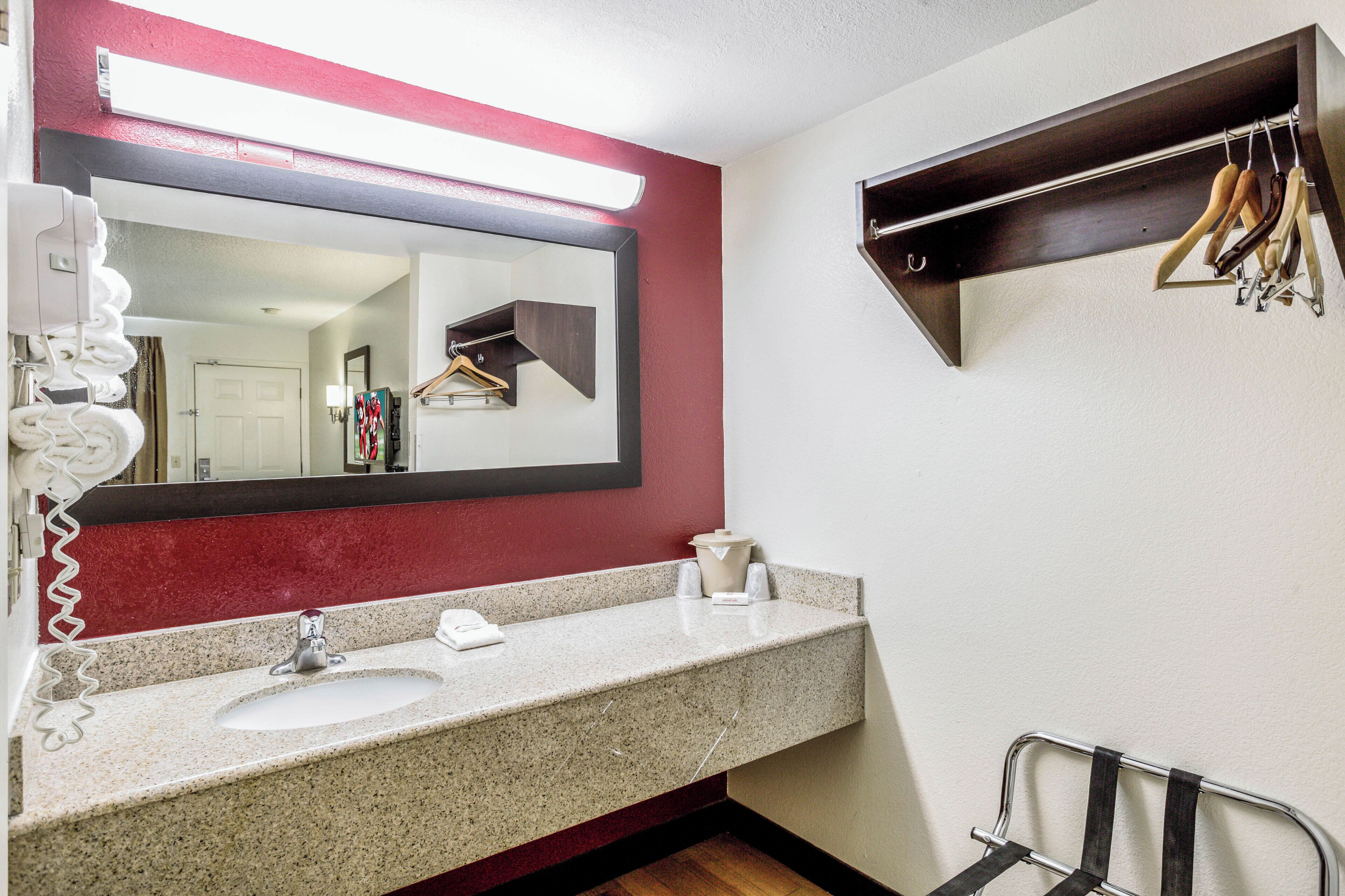 A bathroom with a granite countertop sink, a mirror with a red accent, and a towel rack with multiple towels.