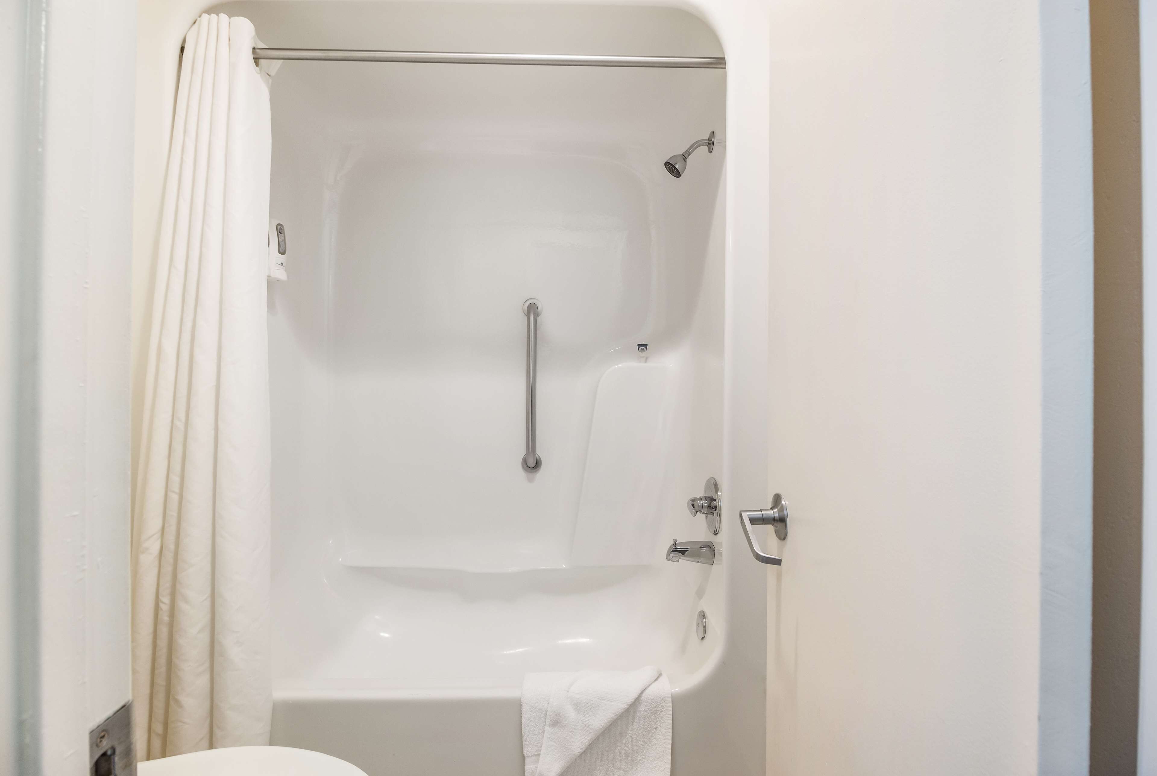 Une baignoire blanche équipée d’une pomme de douche, d’une barre d’appui et d’une serviette.