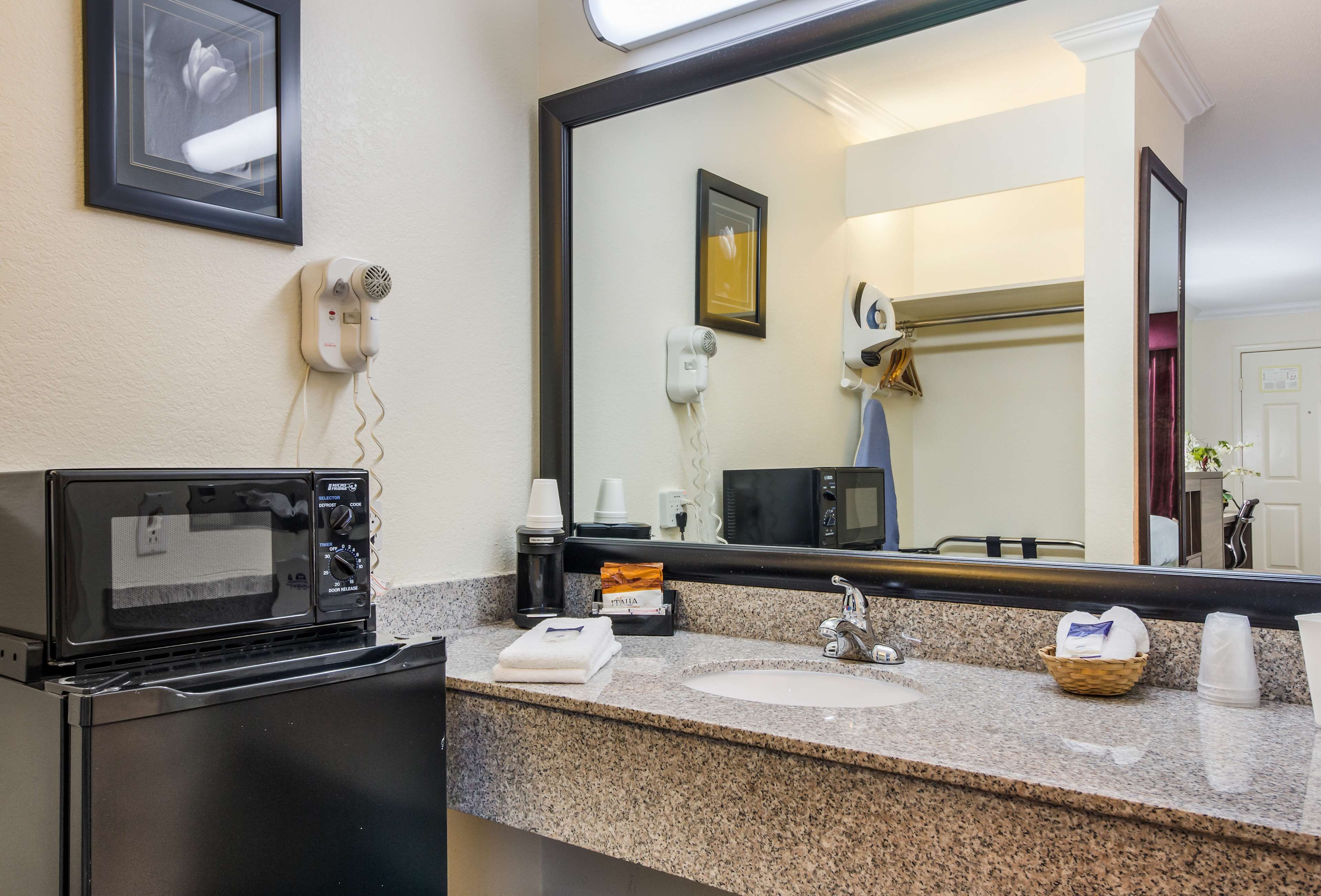 A hotel bathroom with a sink, mirror, and a microwave on the countertop.
