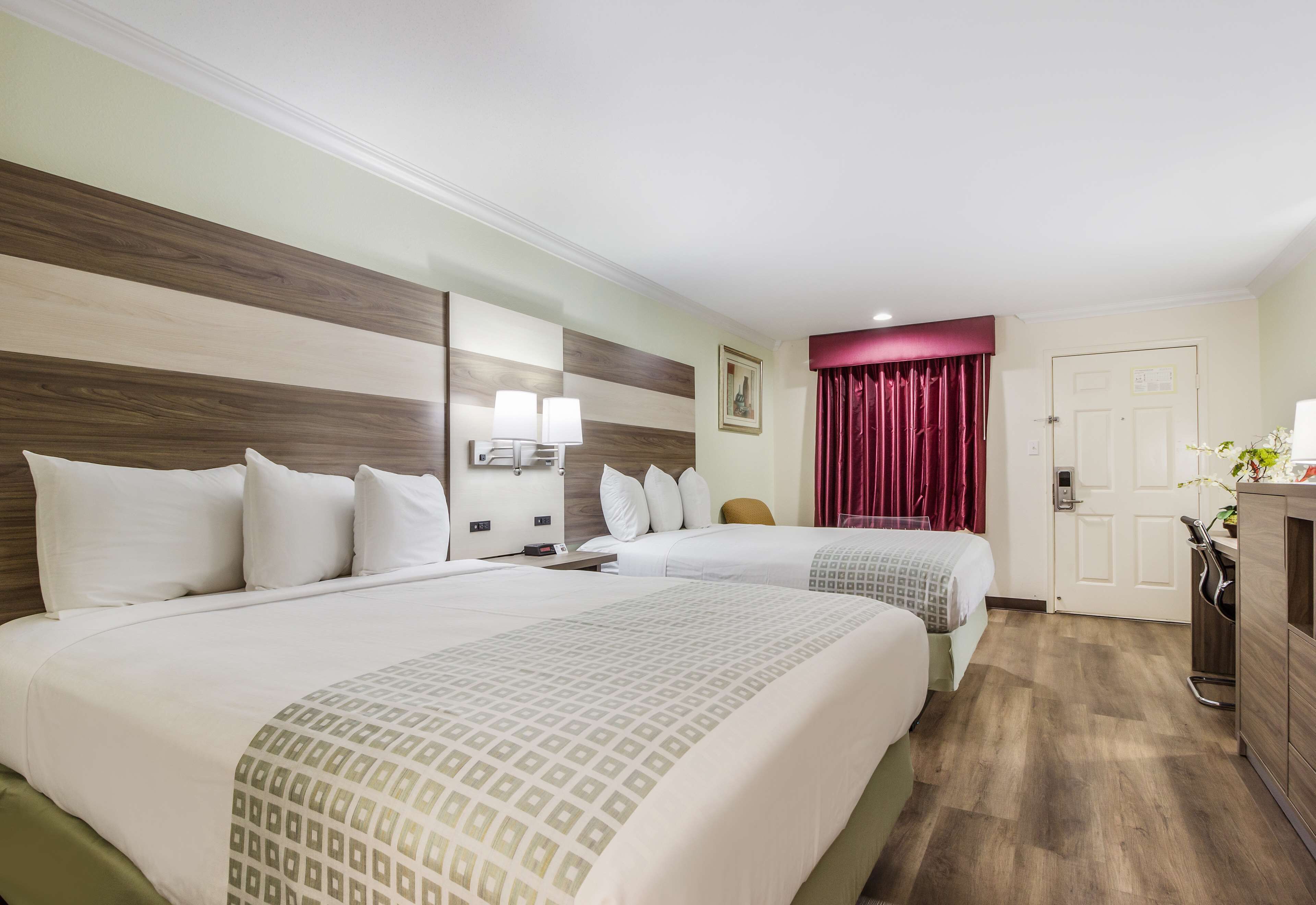 Habitación de hotel con dos camas, un escritorio, una silla, un armario y una puerta.