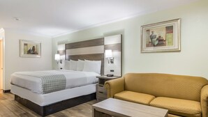 Hotellihuone, jossa on sänky, sohva, yöpöytä lampun kanssa ja kaksi kehystettyä kuvaa seinällä.
