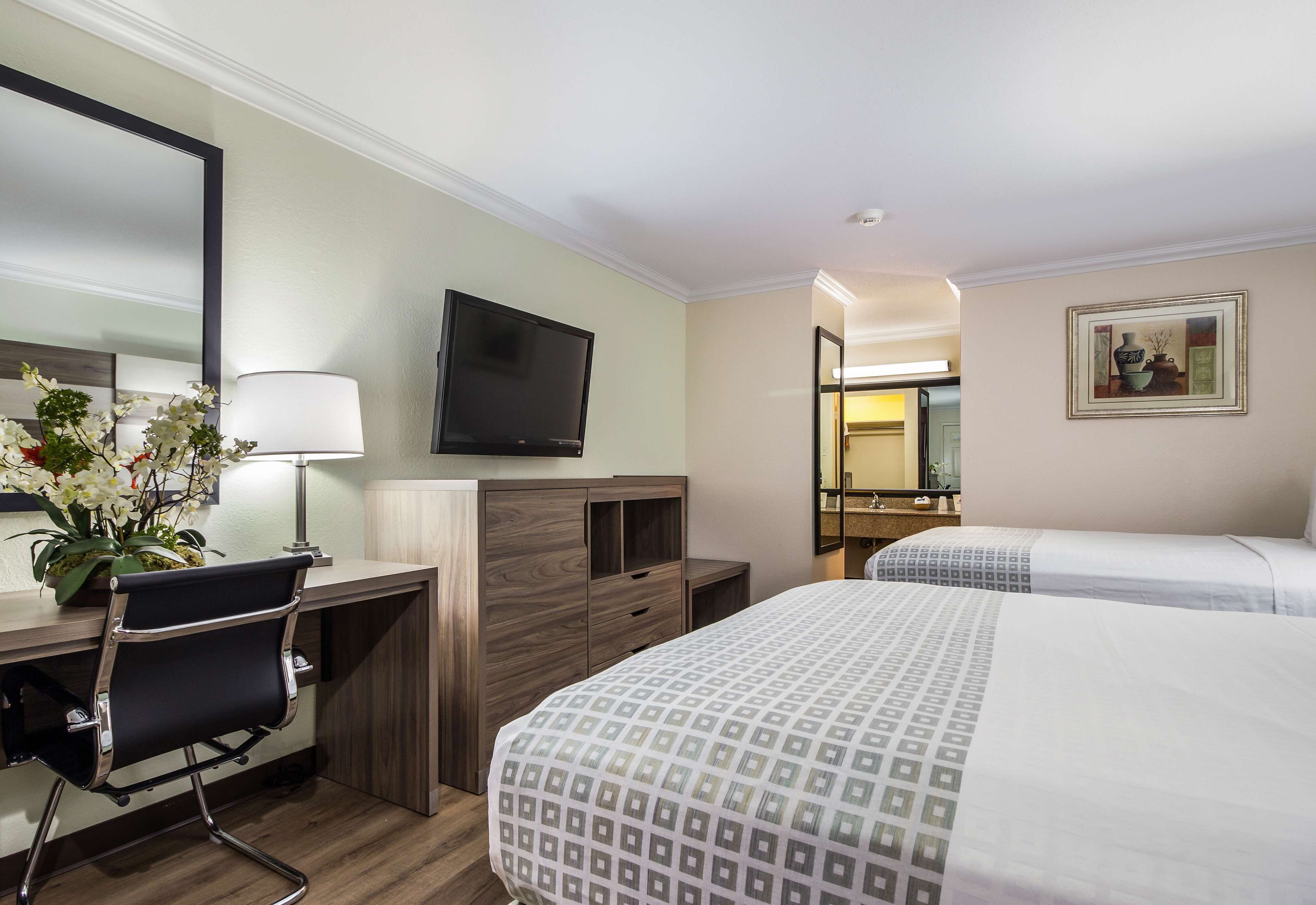 Une chambre d’hôtel équipée d’un bureau, de deux lits, d’une télévision, d’un miroir et d’un tableau au mur.