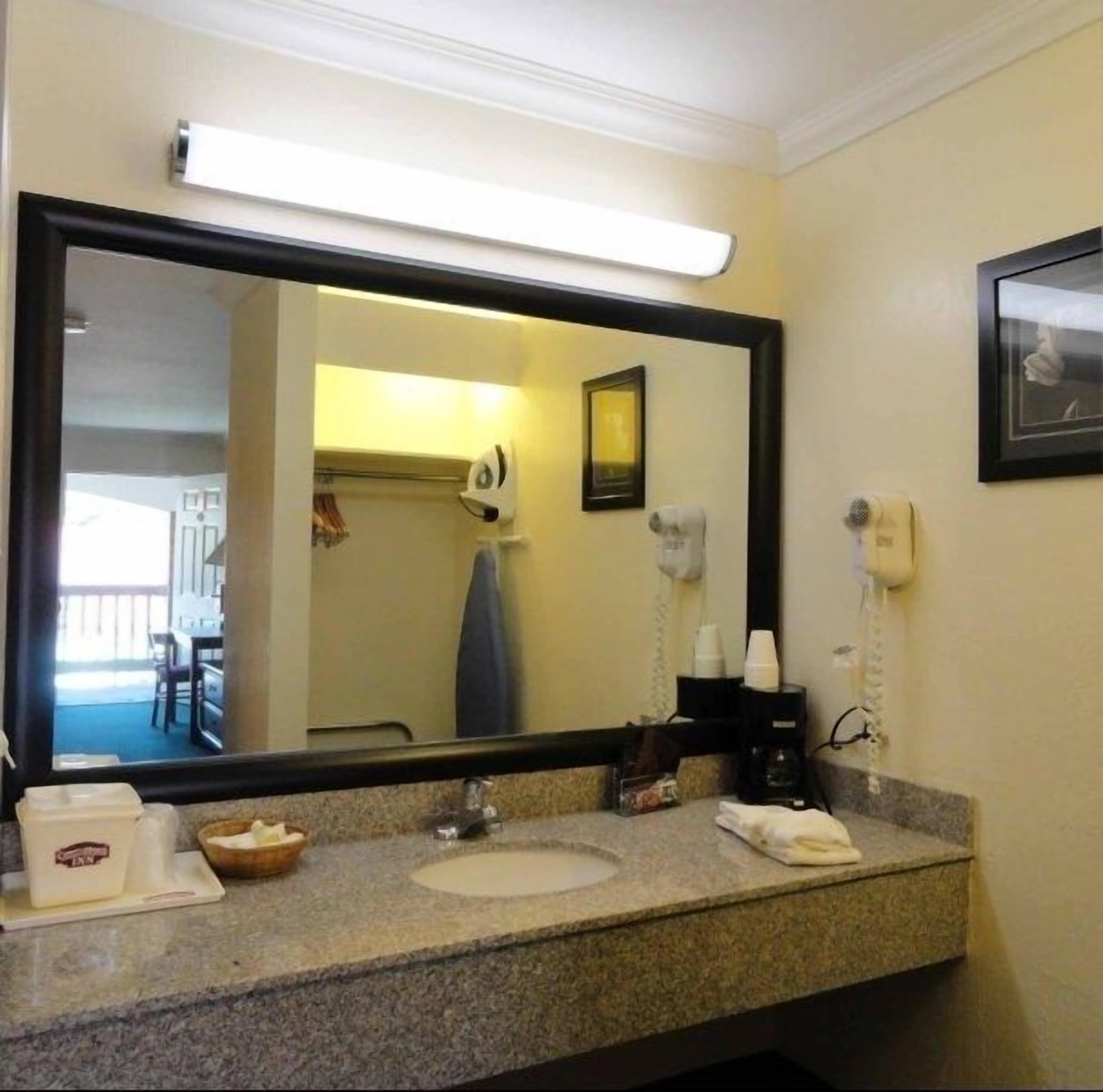 A hotel bathroom with a large mirror, a sink, a towel, a hairdryer, and a phone.