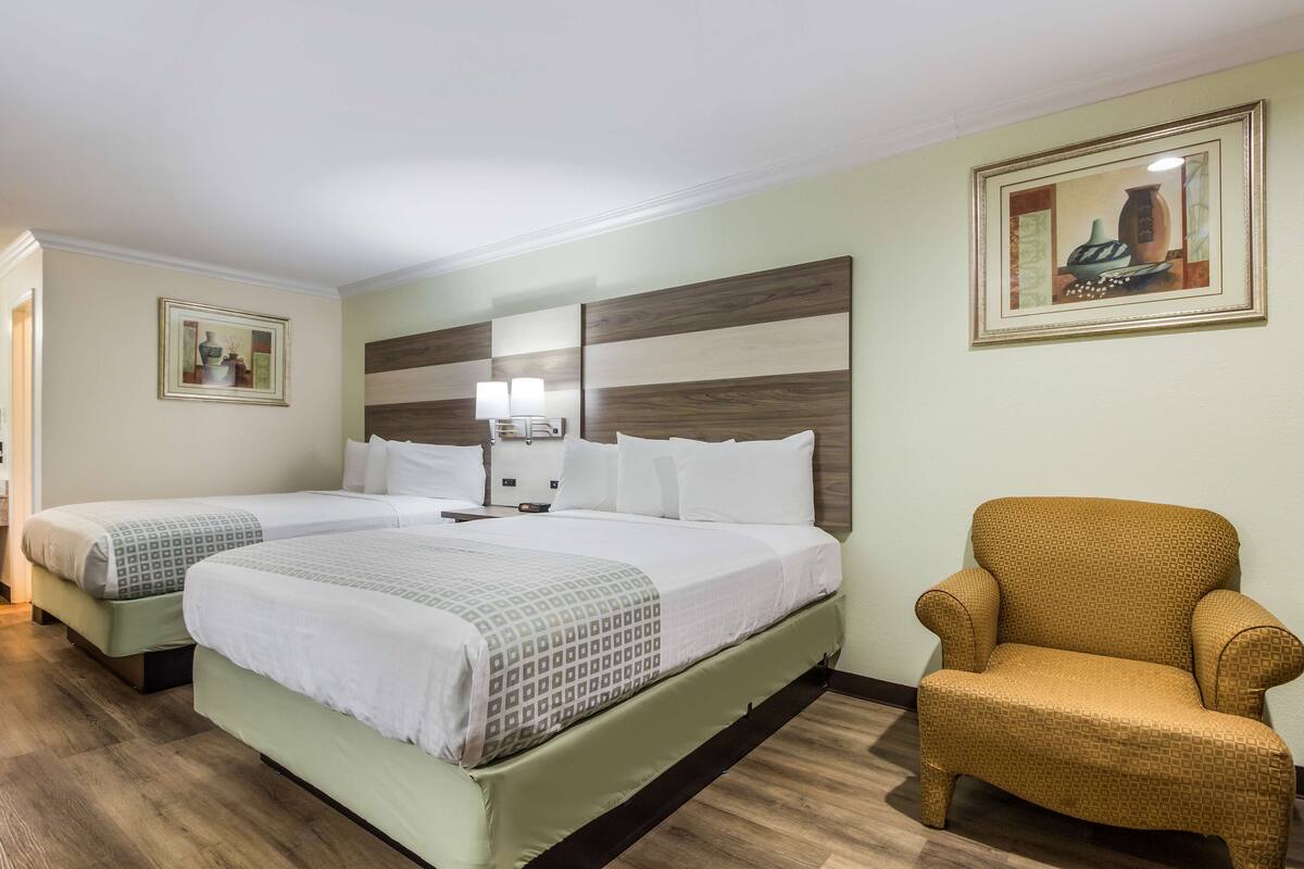 A hotel room with two beds, a nightstand, a lamp, a chair, and artwork on the walls.