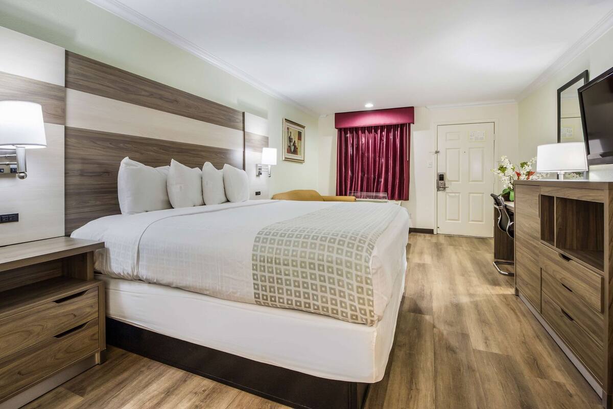 A hotel room with a large bed, bedside tables, a desk, a TV, and a door with a red curtain.