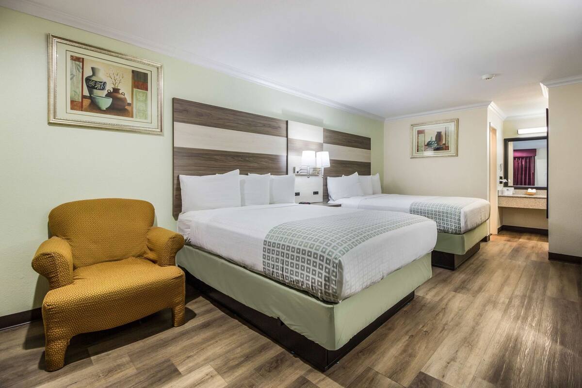 A hotel room with two beds, a chair, a headboard, and artwork on the walls.