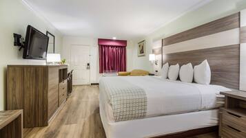 A hotel room with a large bed, wooden furniture, a television, and a red curtain.