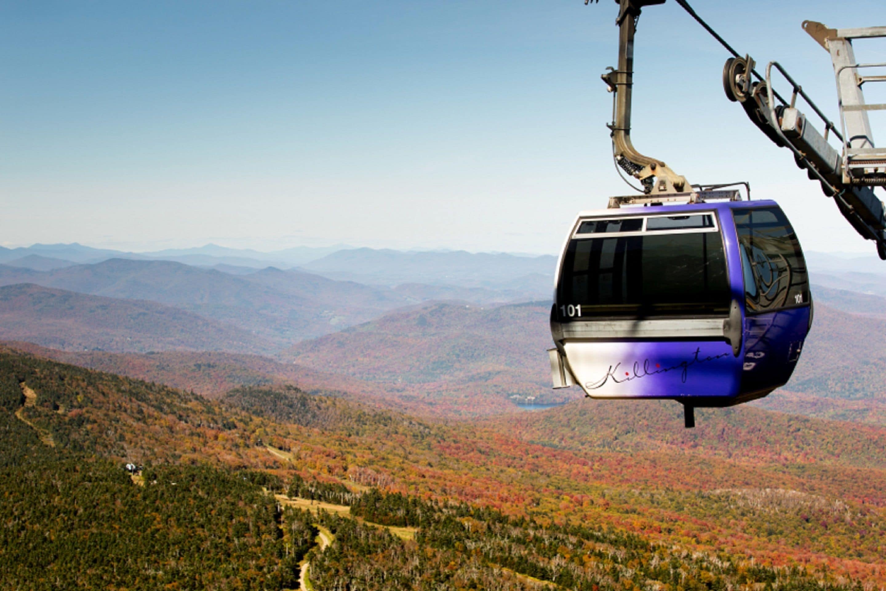 A cable car suspended over a mountainous landscape with autumn foliage.