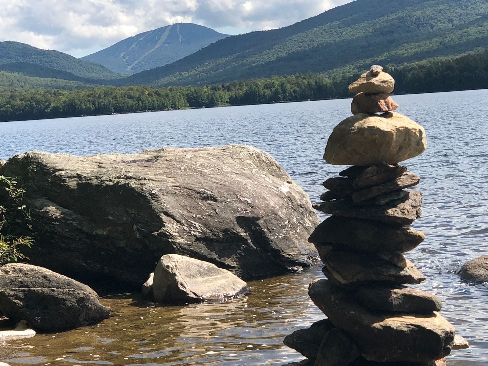 Una pila de rocas junto a un lago, con montañas al fondo.