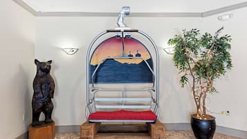 A room with a ski lift chair, a bear statue, and a potted plant.
