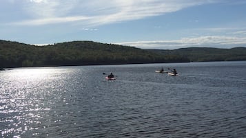 Un lago tranquilo con kayaks y una colina boscosa al fondo.