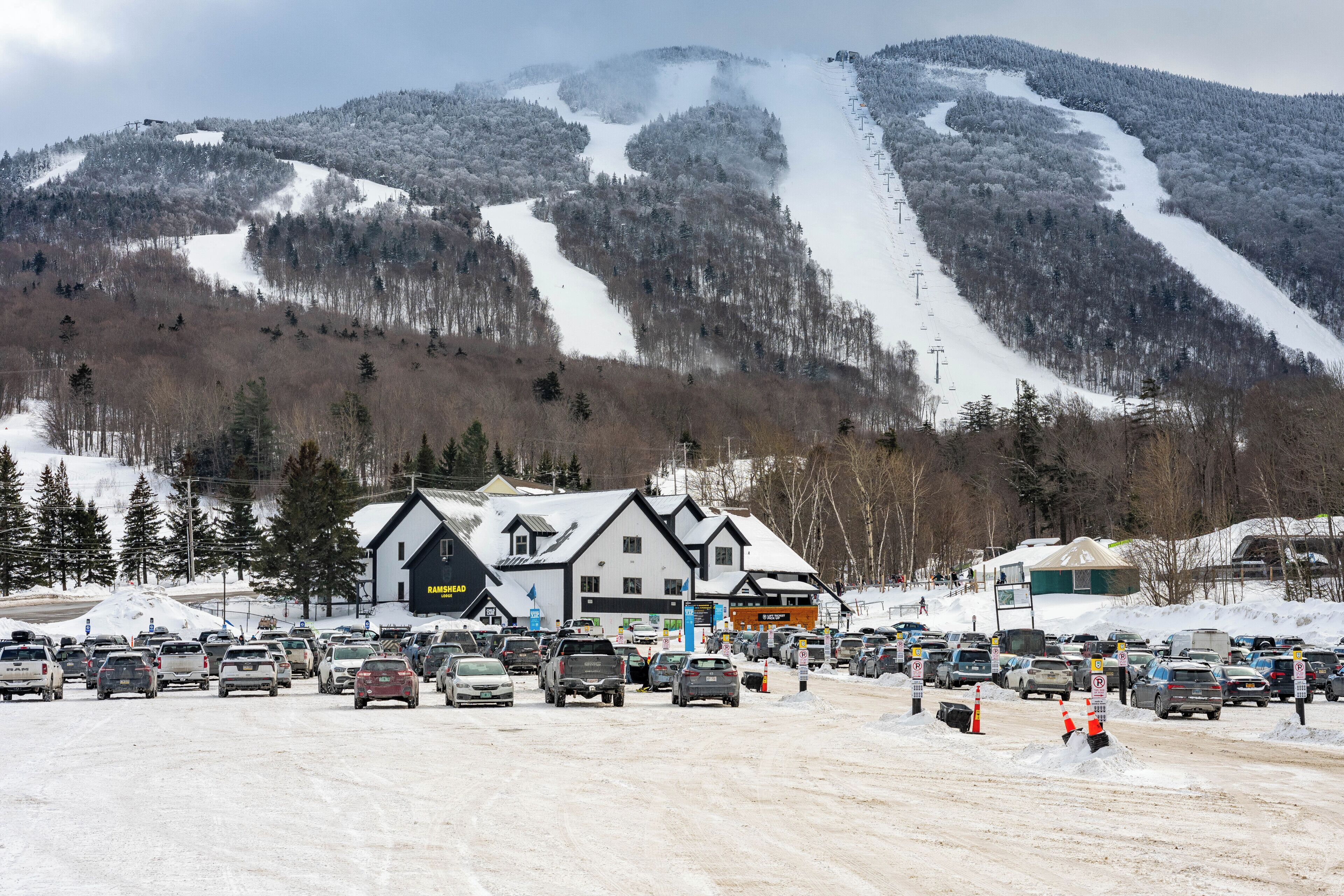 A parking lot with cars, a building with a sign 'RAMS HEAD,' and a snowy mountain in the background.