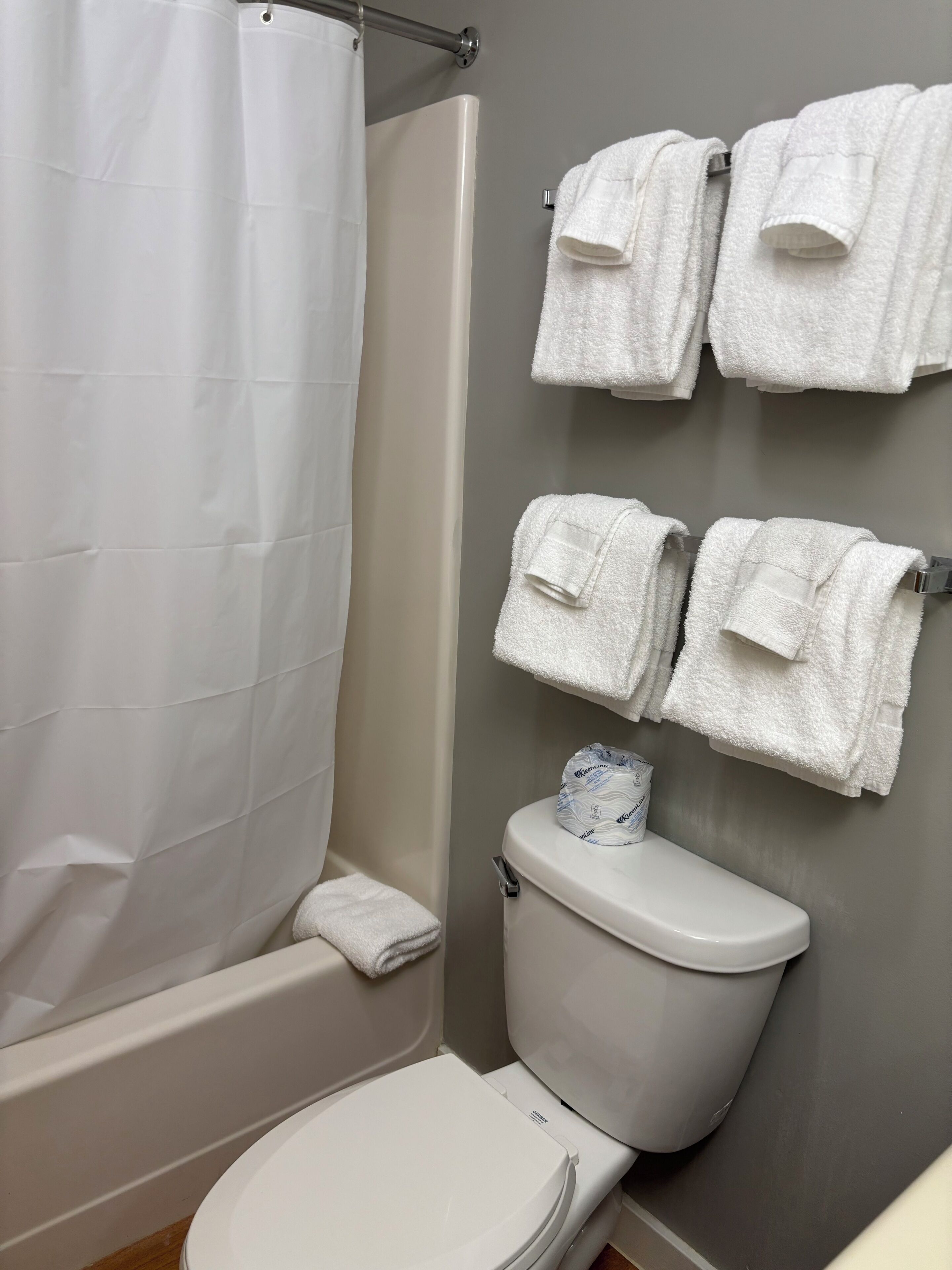 Un baño con inodoro blanco, cortina de ducha y varios toallas blancas colgadas en un perchero.