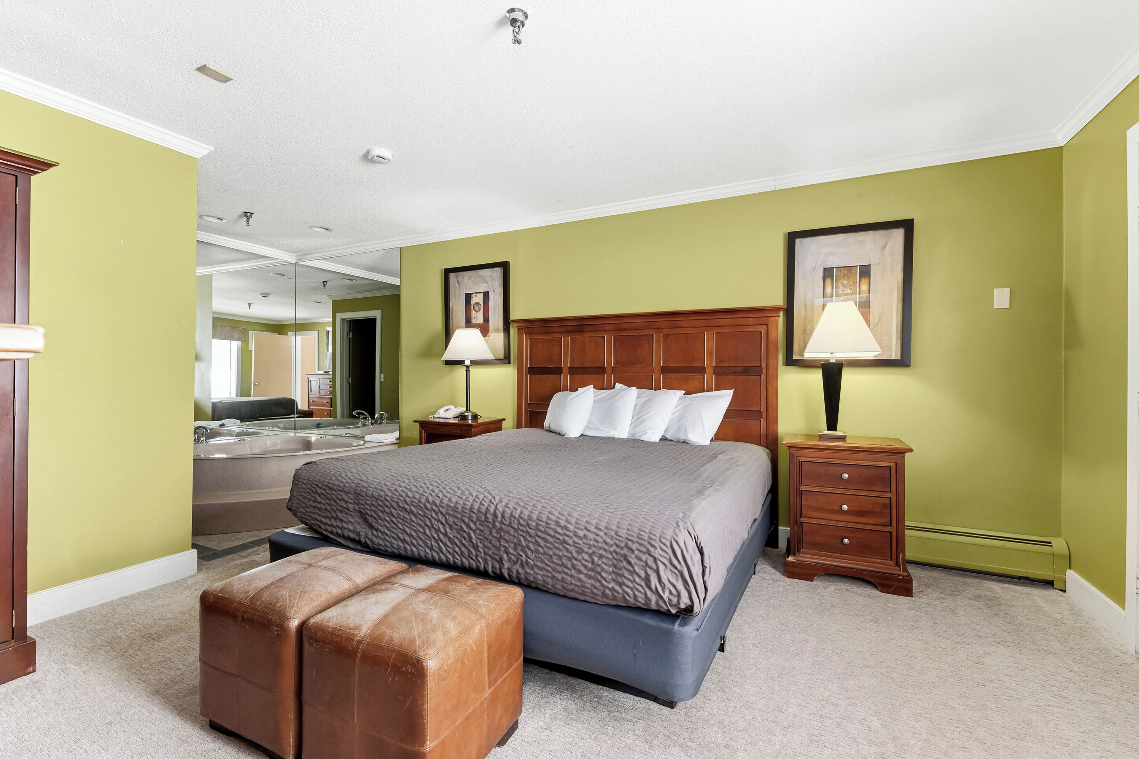 Un dormitorio con una cama grande, una mesita de noche de madera, una lámpara, un banco y un espejo.