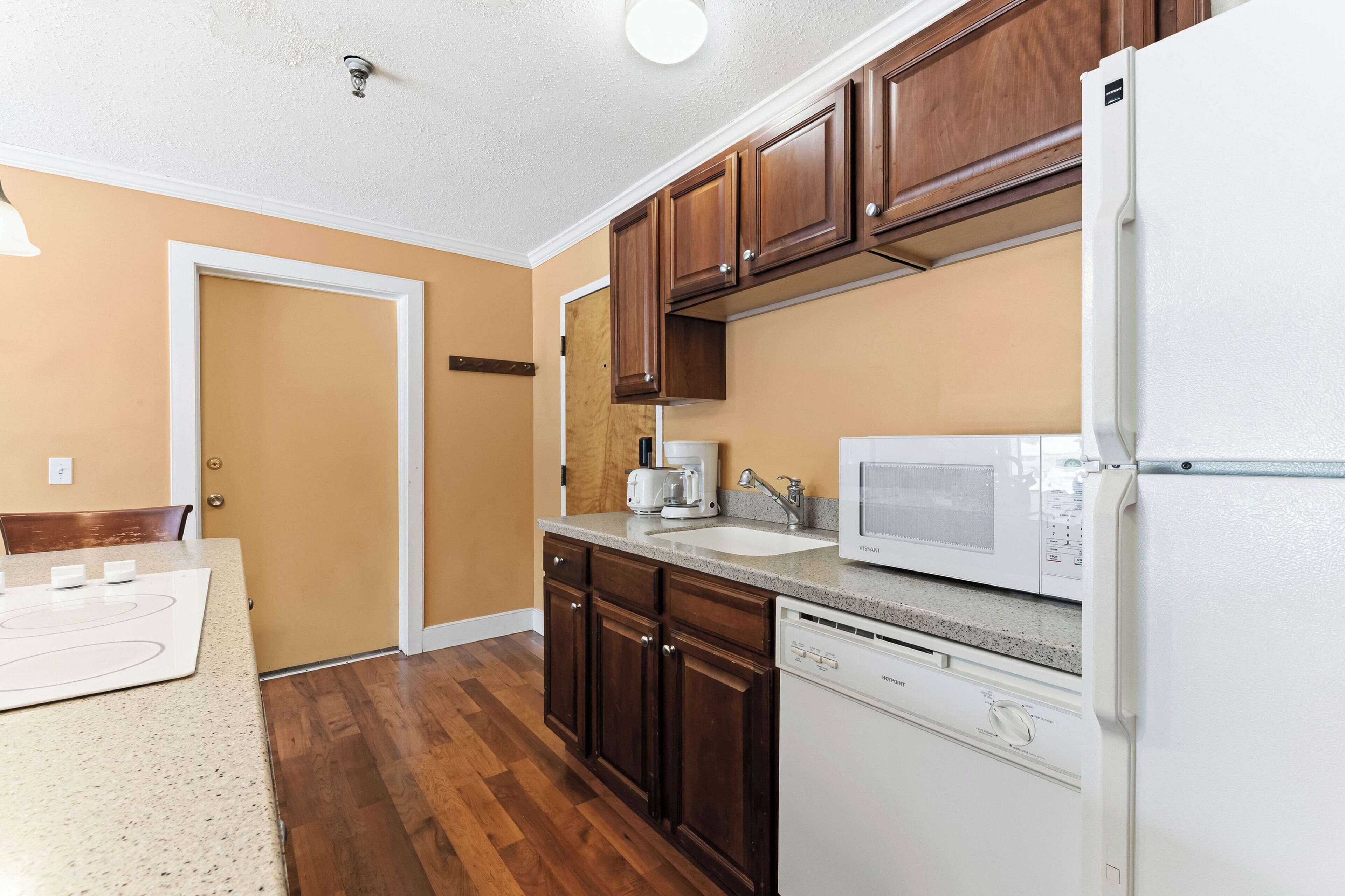 A kitchen with wooden cabinets, a white refrigerator, a microwave, a dishwasher, and a countertop with a coffee maker.
