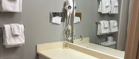 A bathroom with a toilet, sink, mirror, and hairdryer.