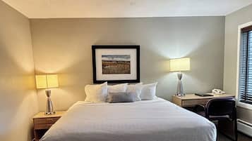 Habitación de hotel con una cama grande, dos lámparas de noche, un escritorio con una silla y un cuadro en la pared.