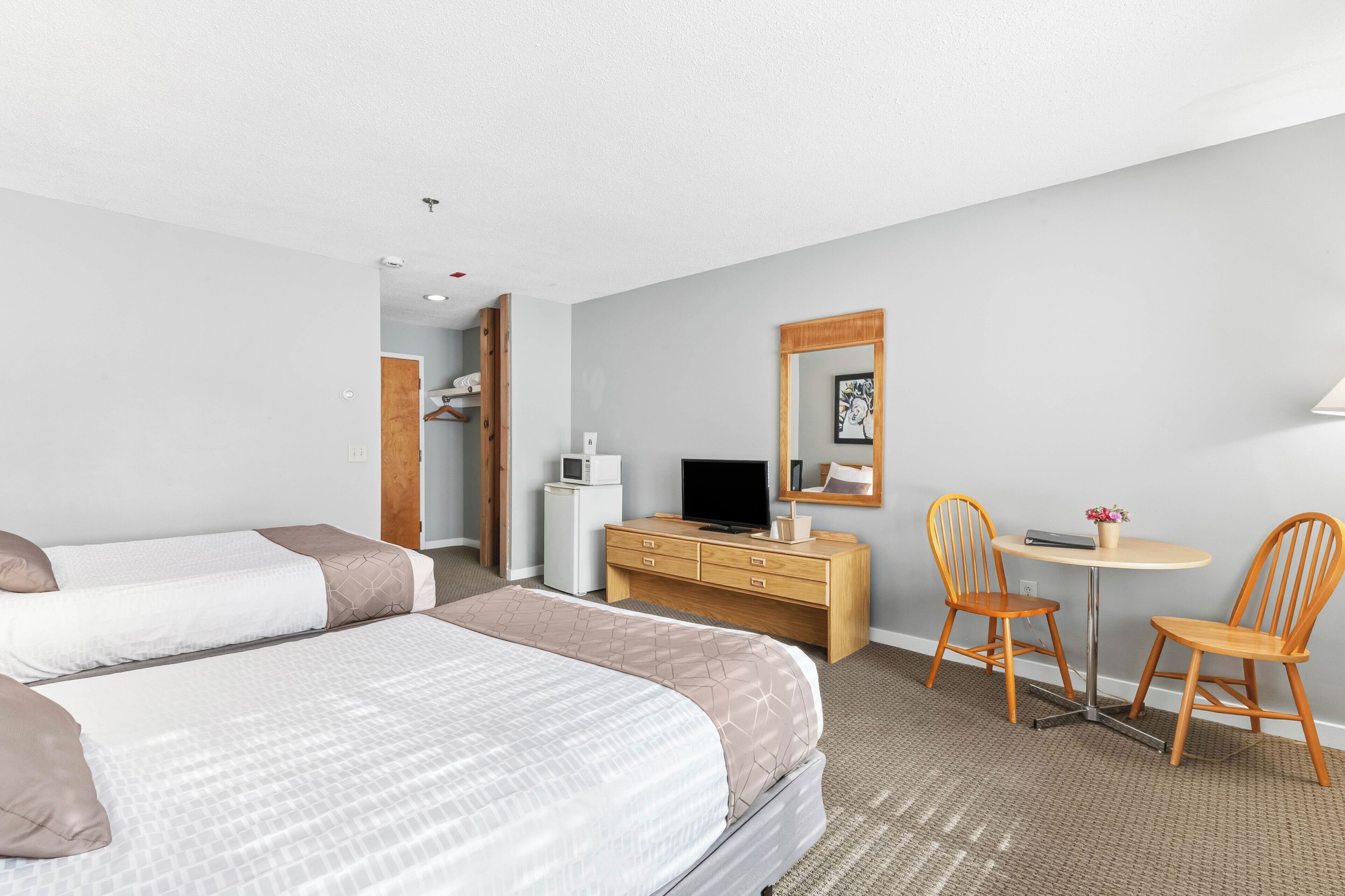 Habitación de hotel con dos camas, un escritorio y una silla, un televisor y una mesita con un florero.