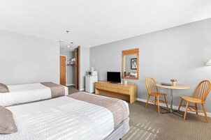 Habitación de hotel con dos camas, un escritorio y una silla, un televisor y una mesita con un florero.