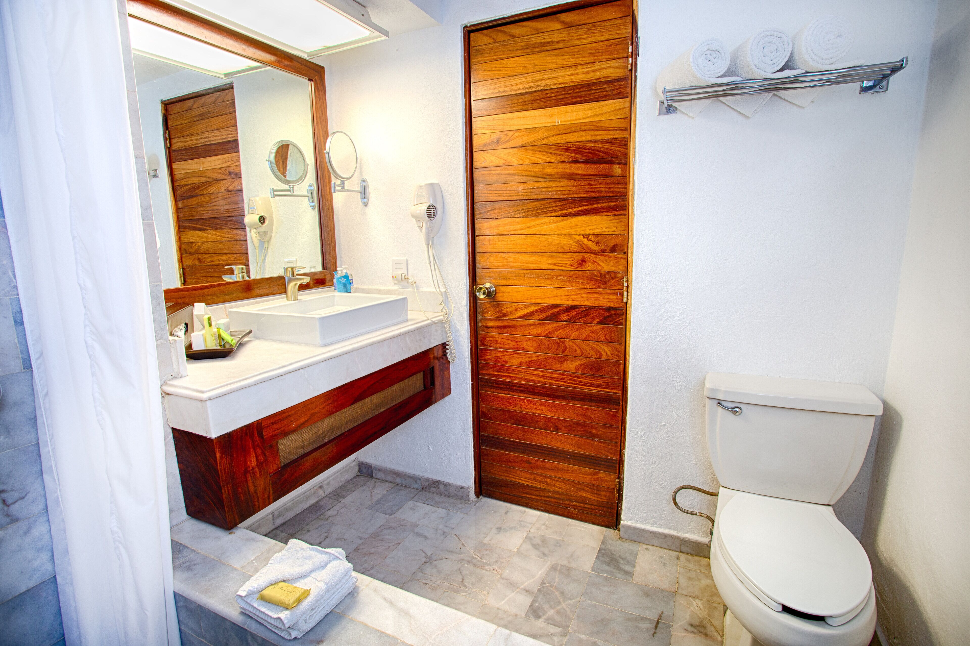 Ein Badezimmer mit Holztür, Waschbecken, Spiegel und Toilette.