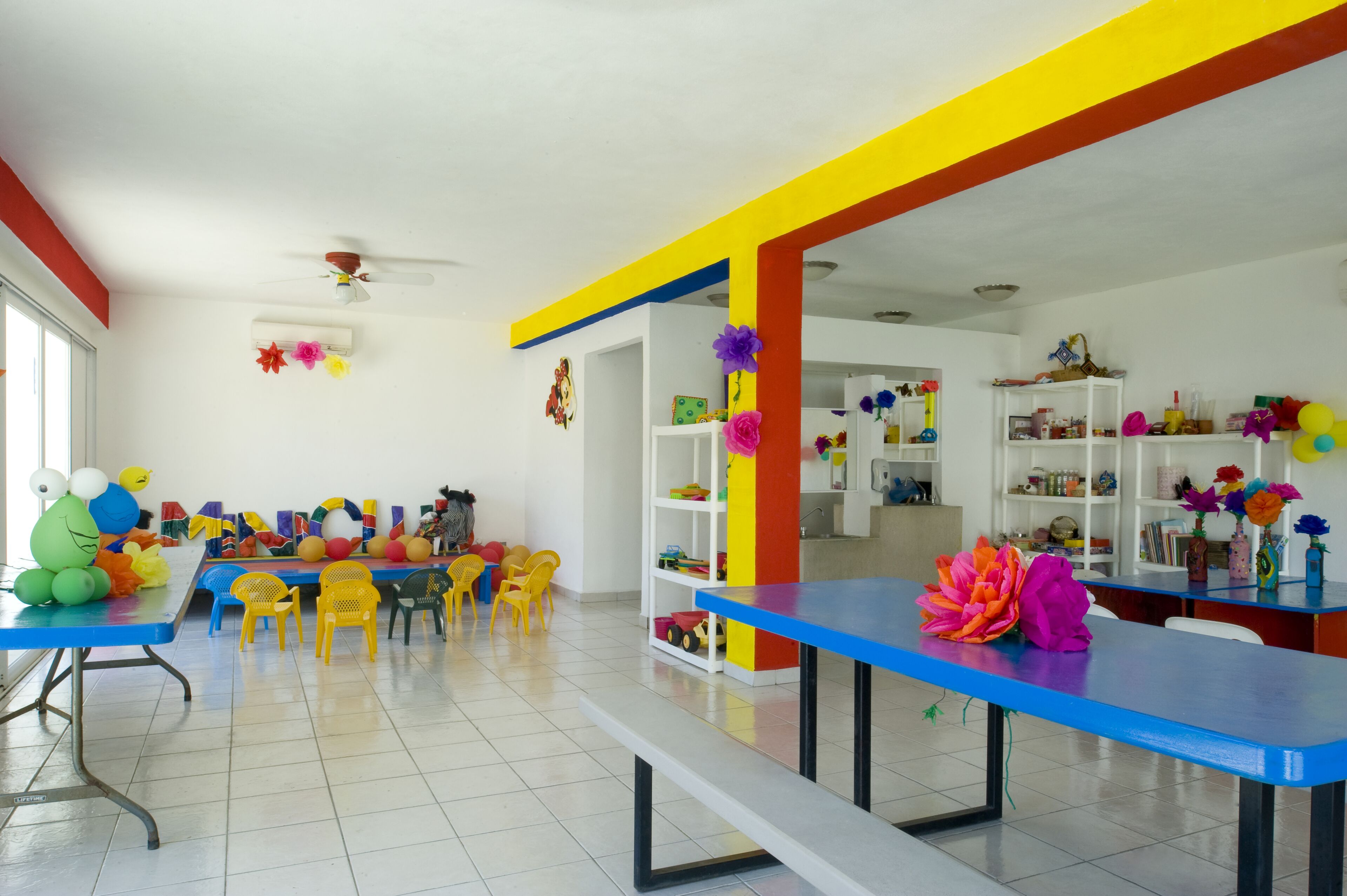 A brightly colored room with a blue table, yellow chairs, and a white bookshelf.