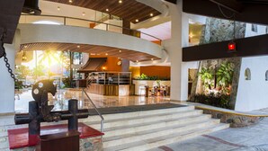 A modern lobby with a central staircase, a reception area, and a view of the outdoor area.