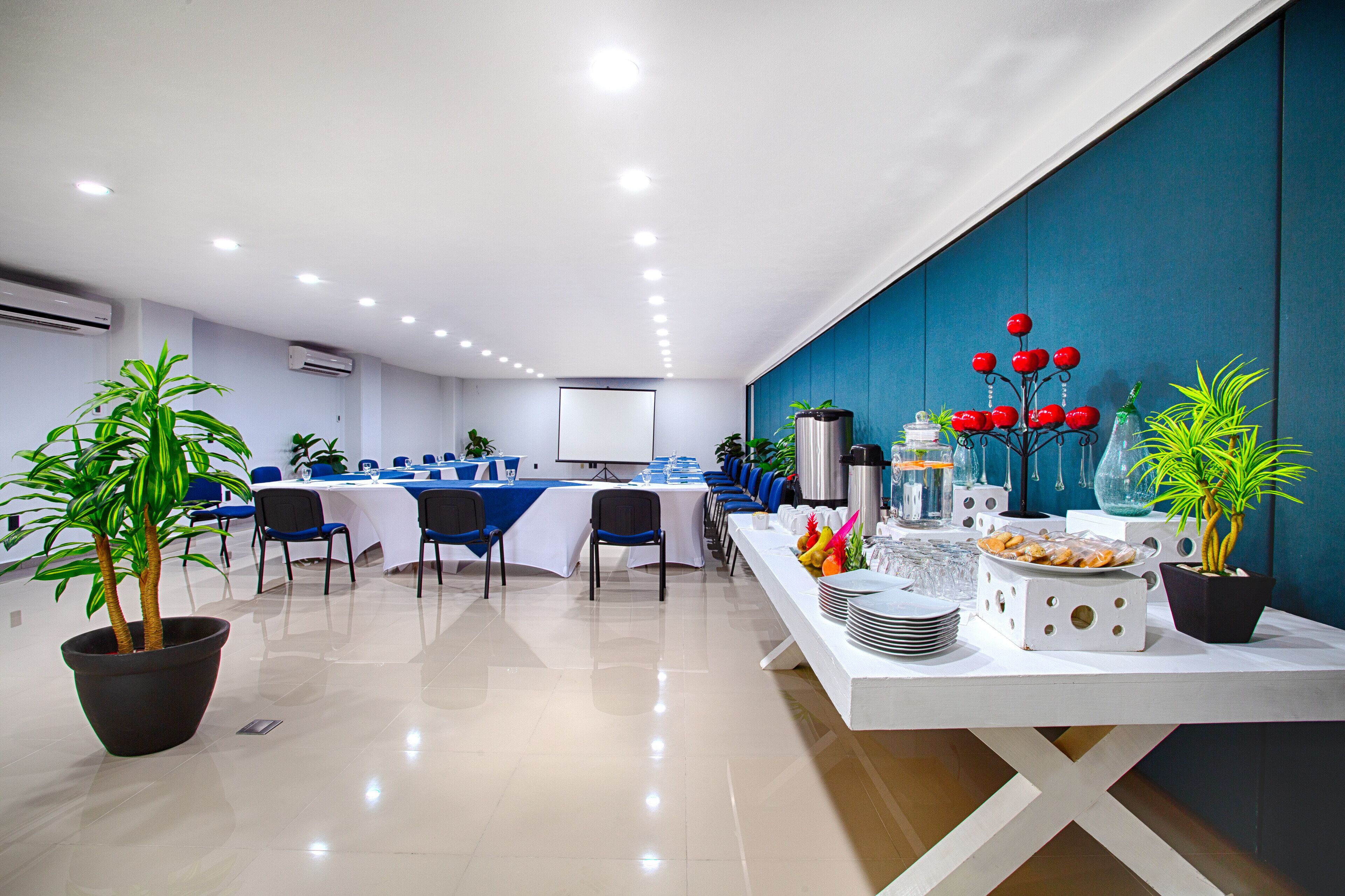 A conference room with a long table, chairs, and a whiteboard. There are potted plants and a buffet table with food and drinks.