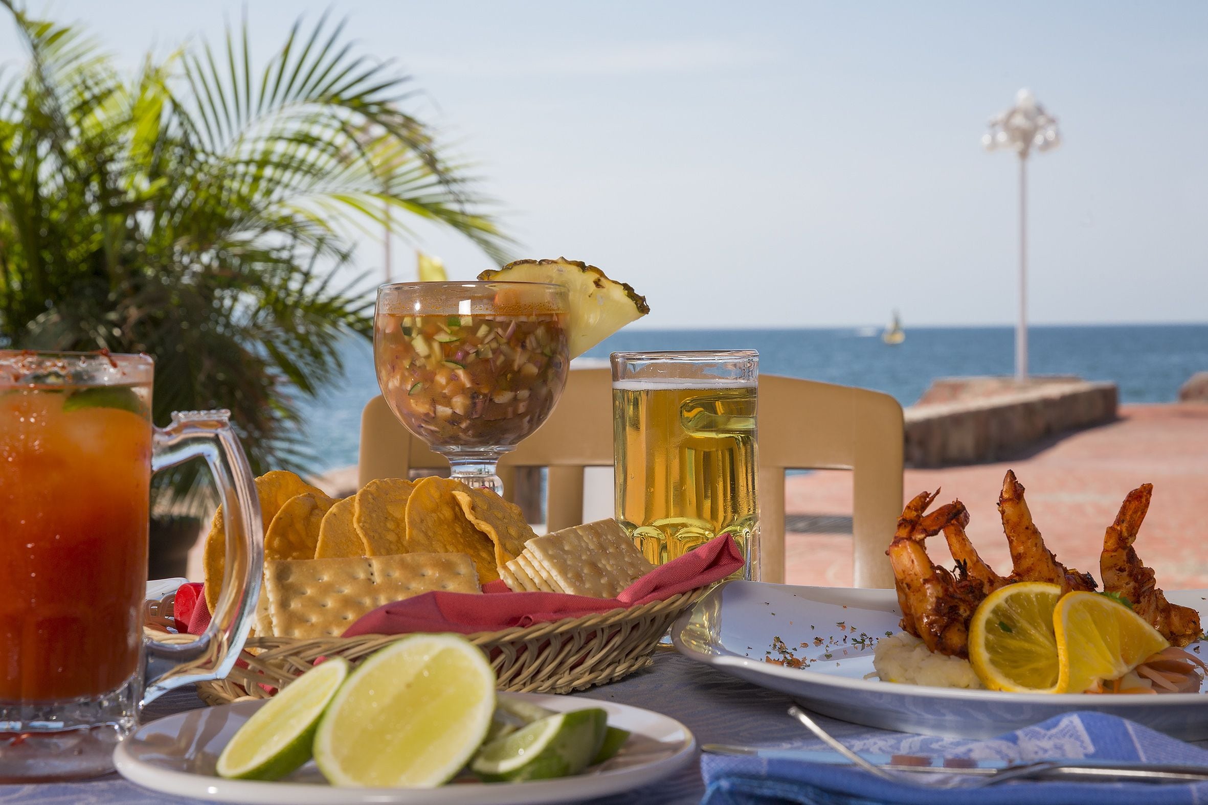 A table set with a drink, snacks, and seafood, overlooking the sea.