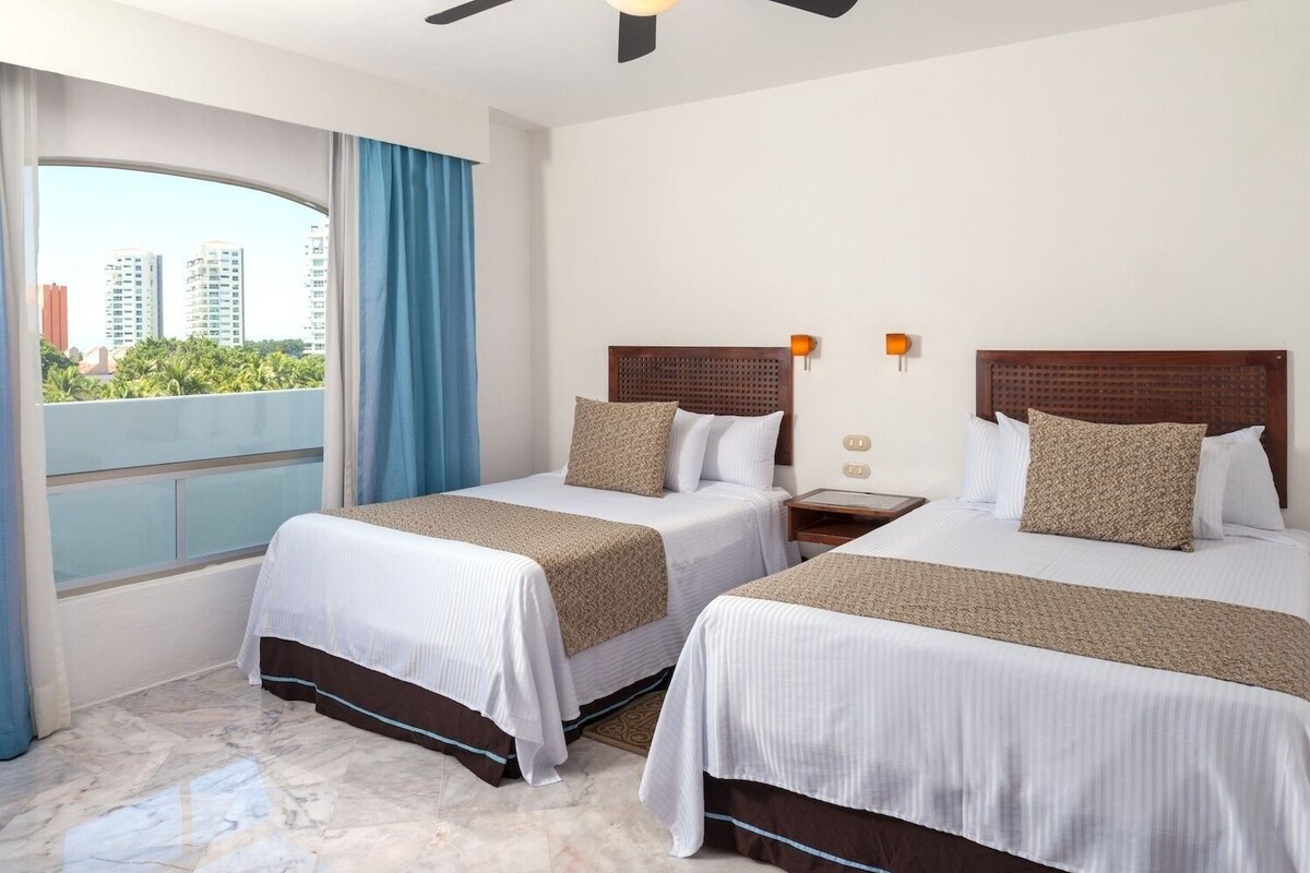 Habitación de hotel con dos camas, balcón y vista a la ciudad.