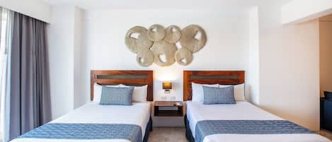 A hotel room with two beds, a ceiling fan, a wall-mounted light, and a decorative wall piece.
