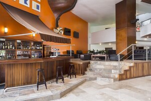 Zona de bar con mostrador de madera, taburetes y una escalera que lleva a un área de estar con sofás de cuero.