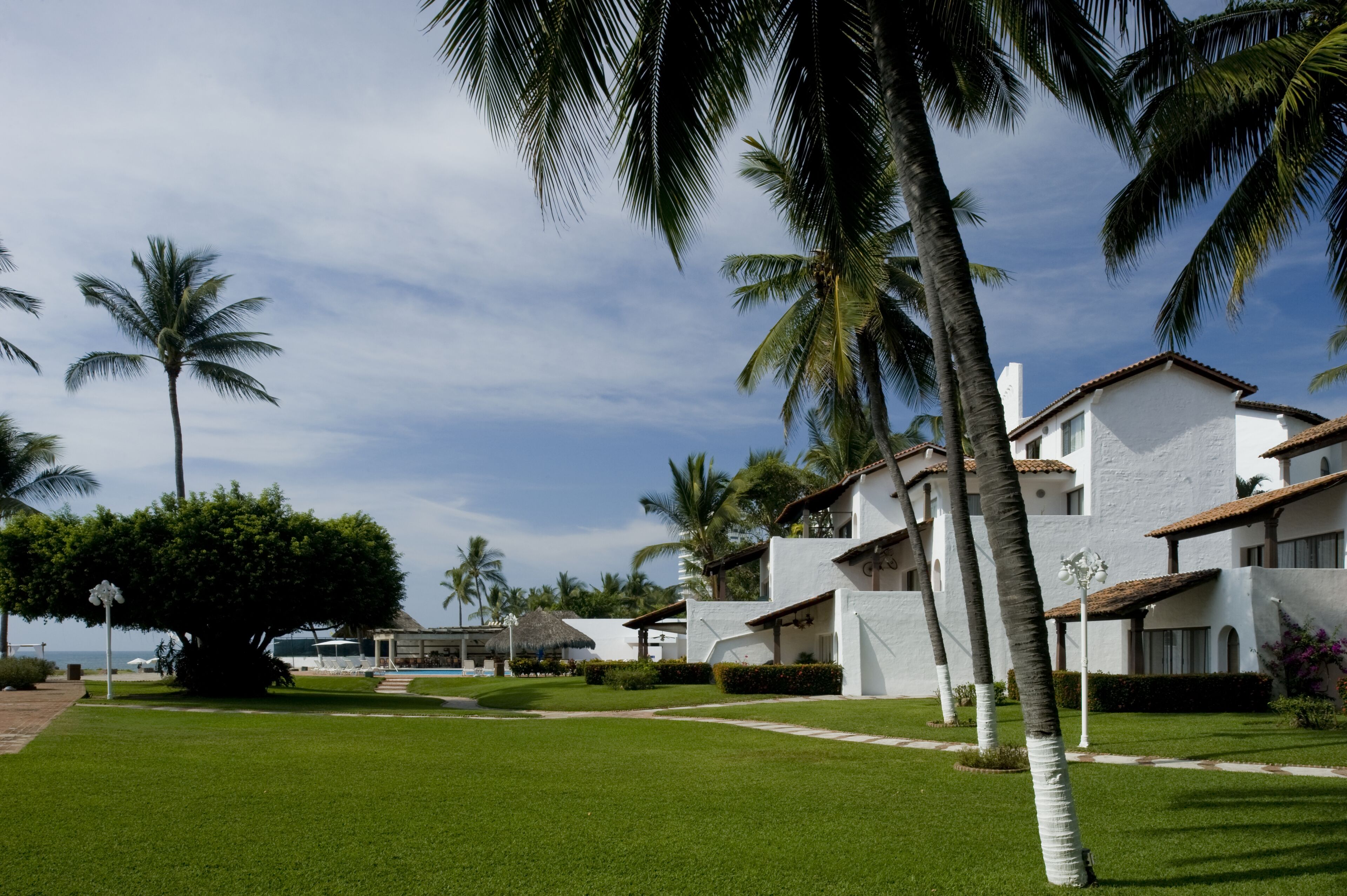 A resort with white buildings, palm trees, and a well-maintained lawn.