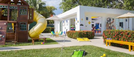 A playground with a slide, a mini-golf course, and a building with colorful murals.