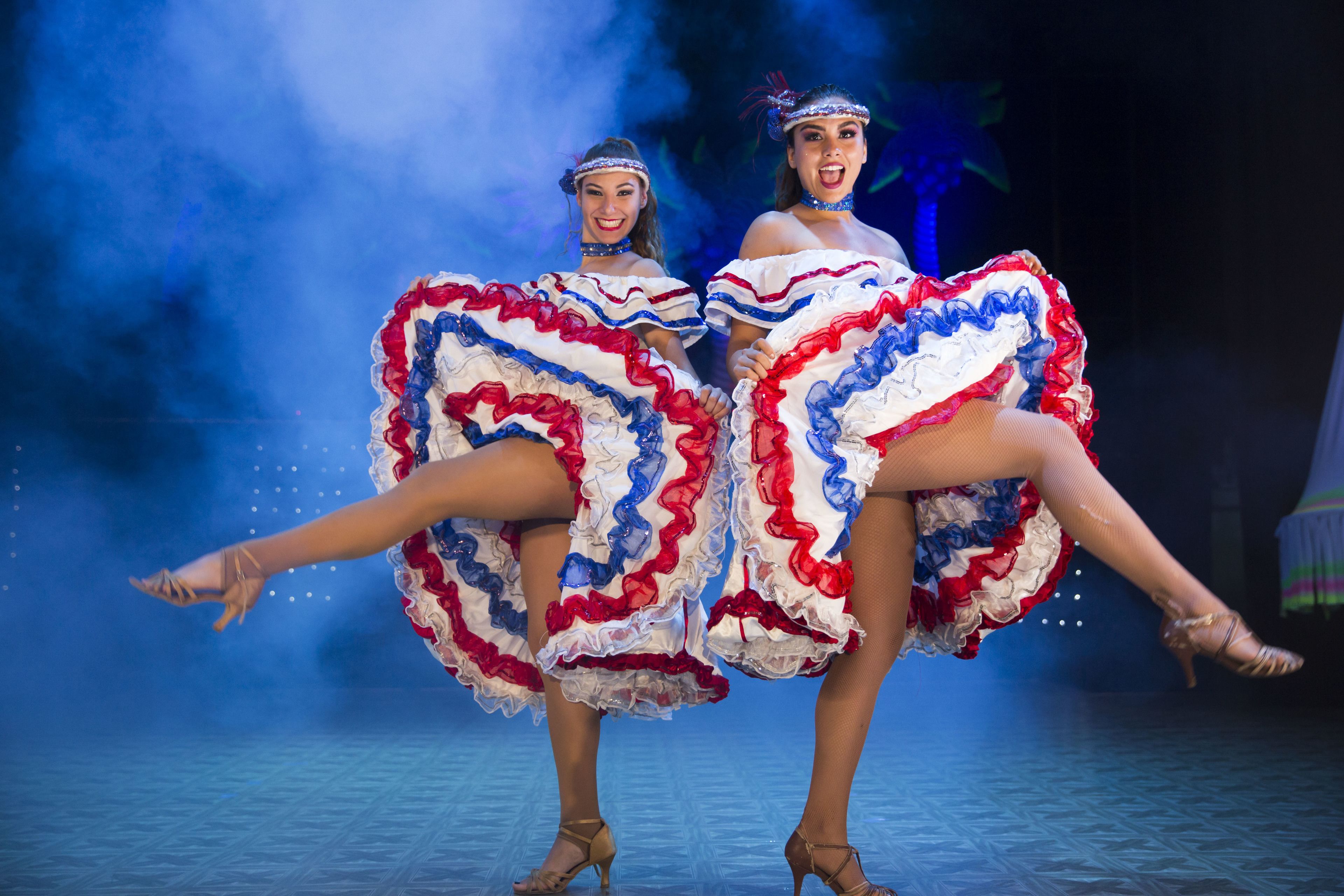 Two dancers in traditional costumes performing on a stage with a blue background.