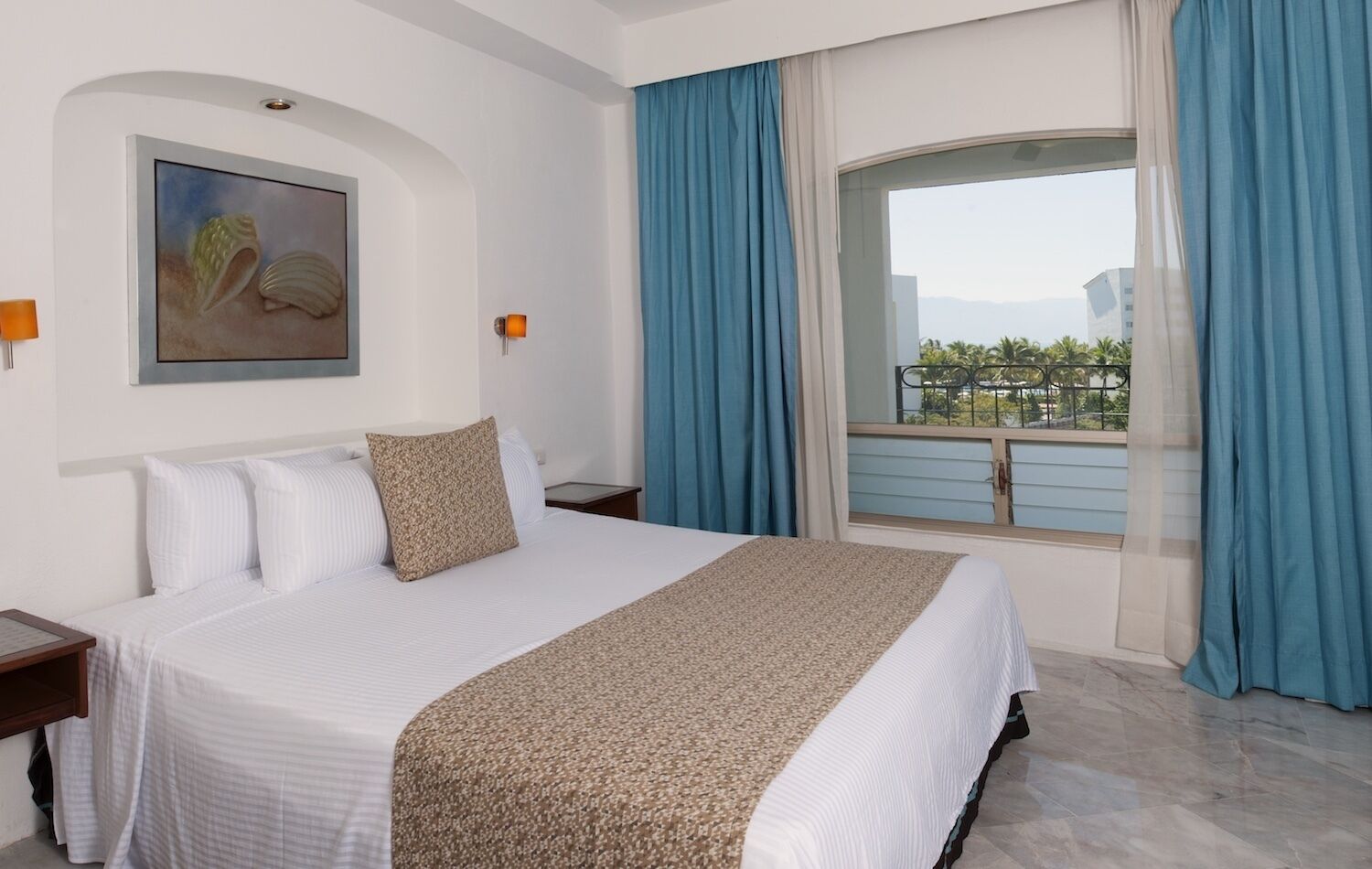 A hotel room with a large bed, a painting on the wall, a window with blue curtains, and a view of the outside.