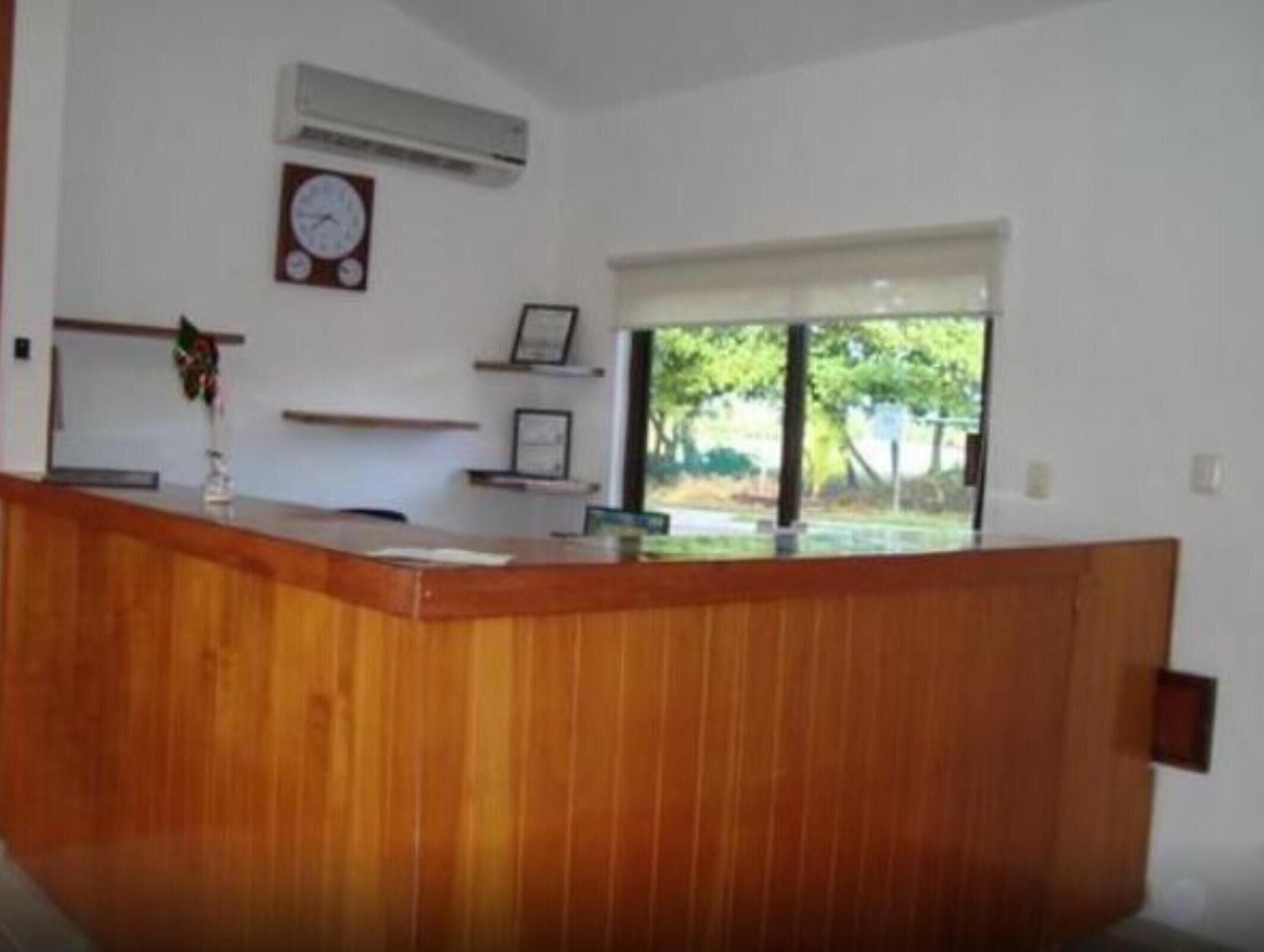 Un comptoir d’accueil avec une horloge, un appareil de climatisation et une fenêtre donnant sur des arbres.