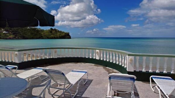 A seaside patio with lounge chairs and a table, overlooking a calm sea and a distant island.