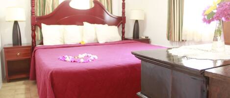 A hotel room with a large bed, two bedside tables, a dresser, and a window with curtains.