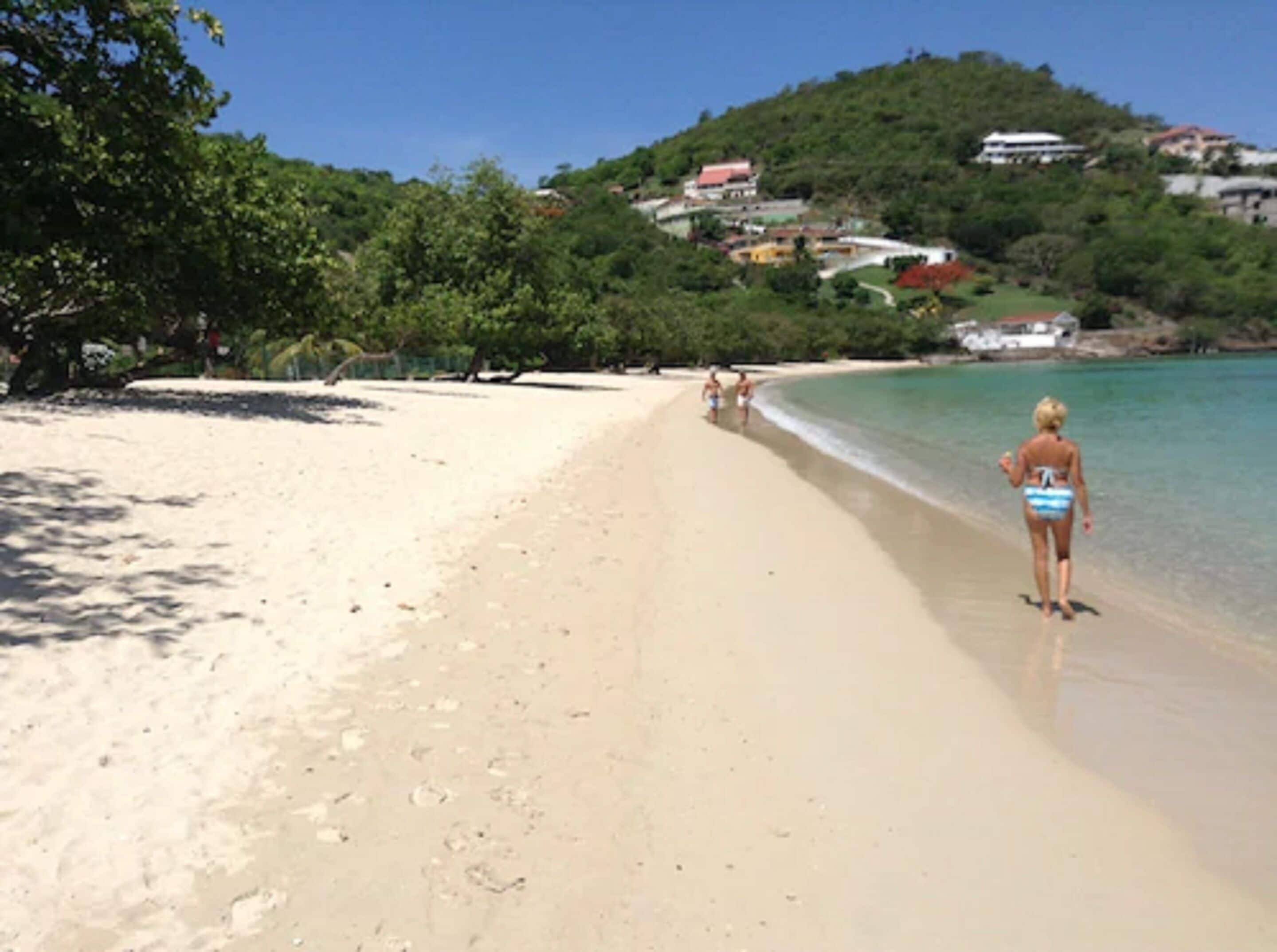 Une plage offrant une vue dégagée sur le littoral, avec quelques personnes qui se promènent et des bâtiments en arrière-plan.