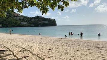 A sandy beach with footprints and a few people in the water.