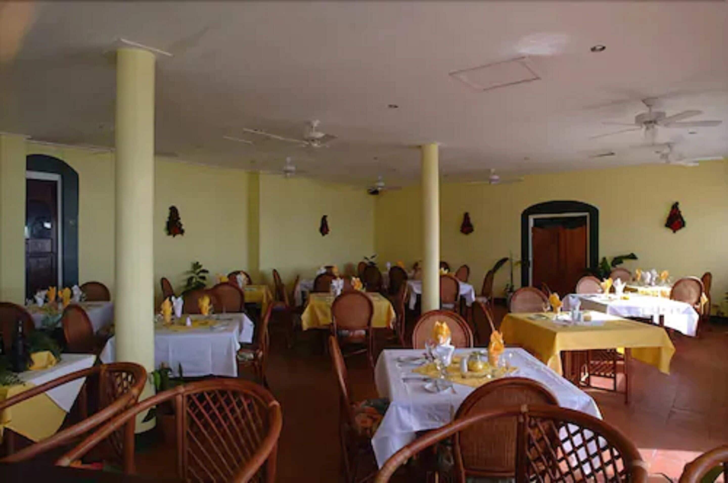 A restaurant with multiple tables and chairs, yellow walls, and ceiling fans.