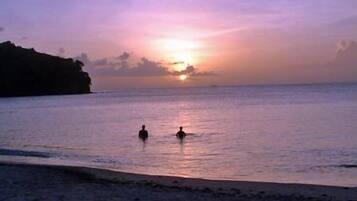 Escena de playa al atardecer con aguas tranquilas y la silueta de un acantilado.