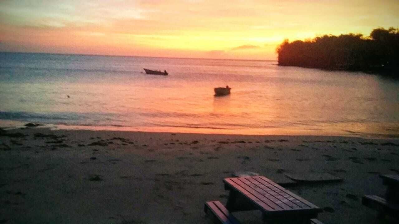 A beach with a wooden picnic table and a boat in the water.
